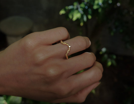 Daphnis Wedding Band — curved vine band worn on a hand outdoors.