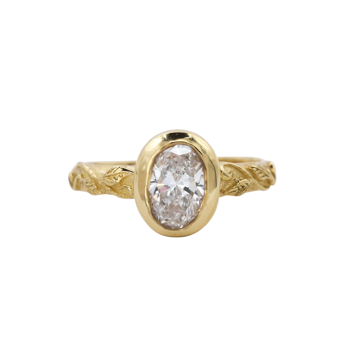 Interlaced Diamond Ring — A colorless oval diamond is bezel-set vertically above a yellow-gold band worked with interlaced leaves and vines.
