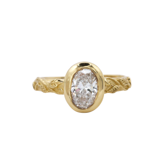 Interlaced Diamond Ring — A colorless oval diamond is bezel-set vertically above a yellow-gold band worked with interlaced leaves and vines.