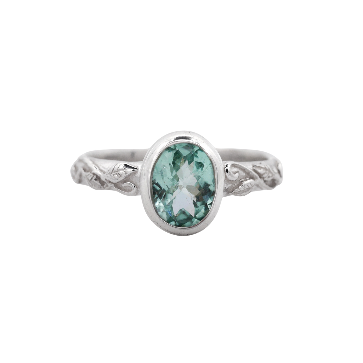 Interlaced Mint Tourmaline Ring — A mint-green oval stone in a smooth silver bezel crowns a narrow band with raised vine and leaf relief.