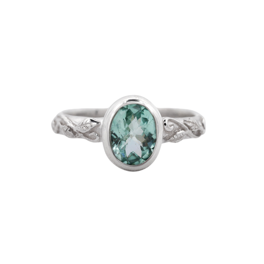 Interlaced Mint Tourmaline Ring — A mint-green oval stone in a smooth silver bezel crowns a narrow band with raised vine and leaf relief.