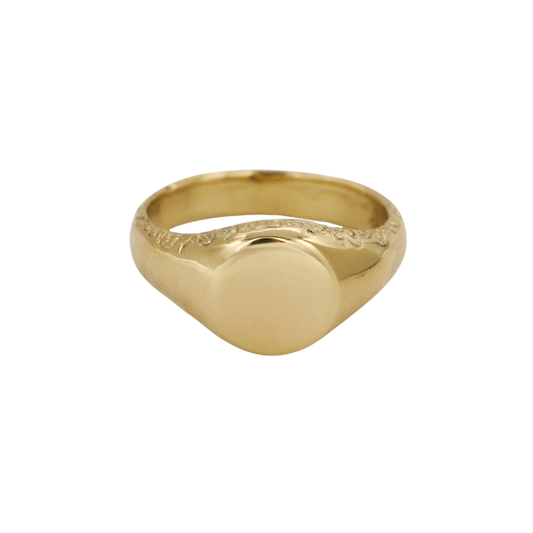 Scribe Signet Ring — A yellow-gold signet ring has a blank rounded face, broad tapered shoulders, and incised scrolling along the upper shank.