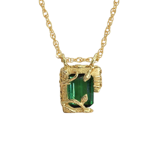 Tourmaline Chamber Pendant — A deep-green rectangular step-cut tourmaline is held in a yellow-gold-colored pendant frame formed from leaves, vines, and irregular sculptural prongs.