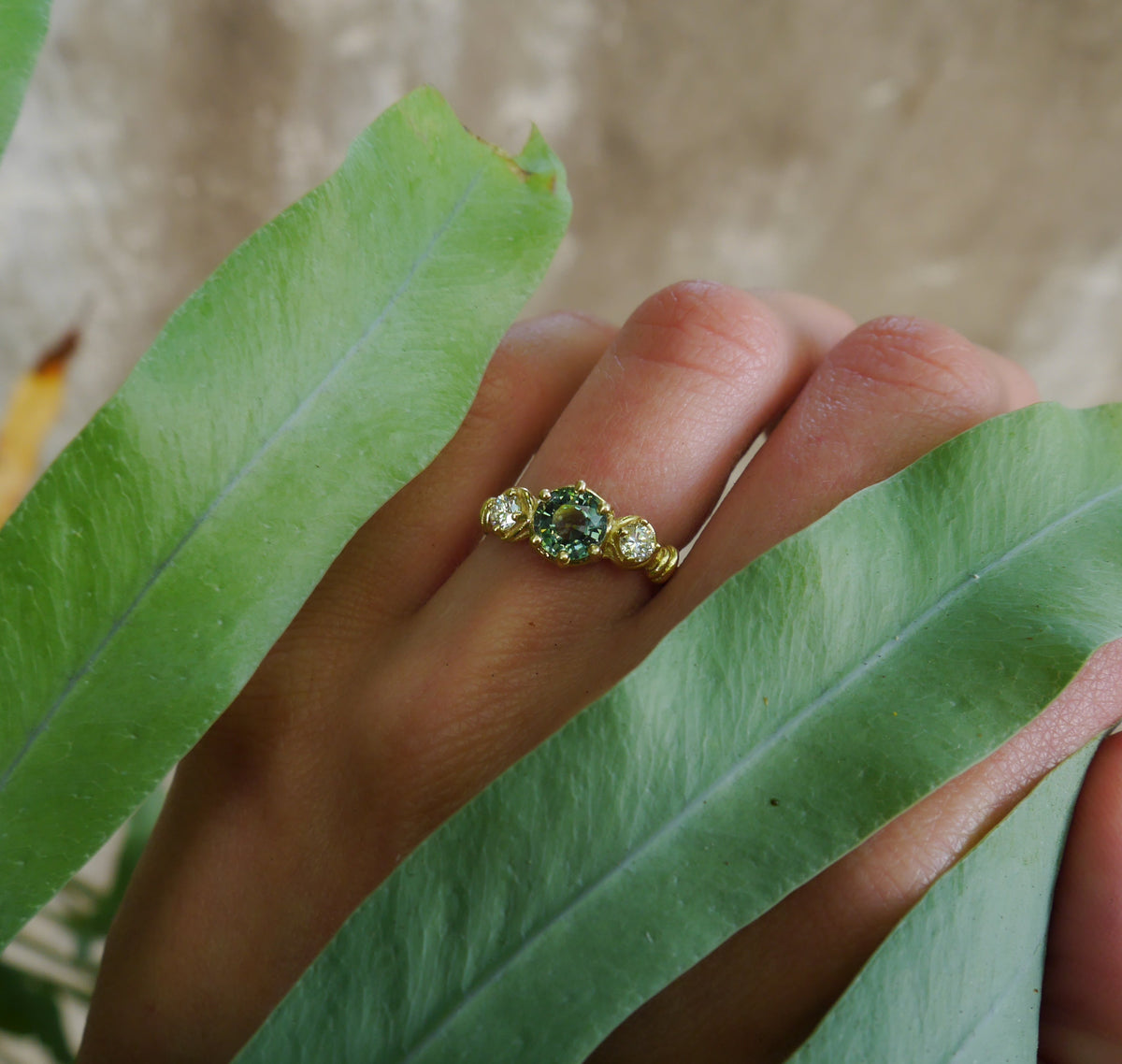 Verdant Ring — worn on a hand framed by green leaves.
